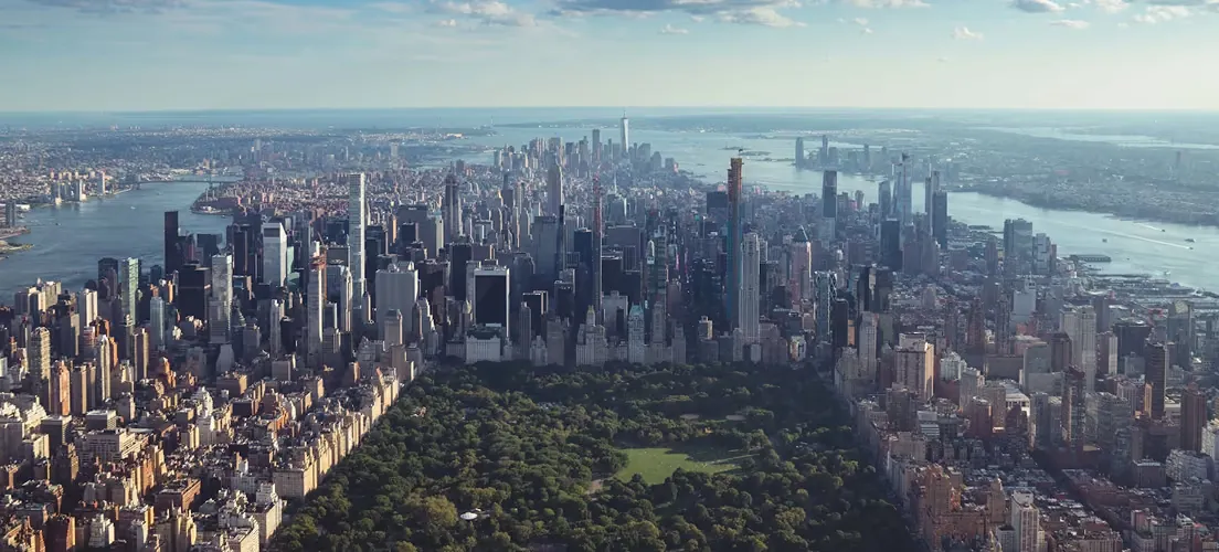Aerial view of Manhattan with Central Park in the foreground and the New York City skyline stretching to the water beyond.