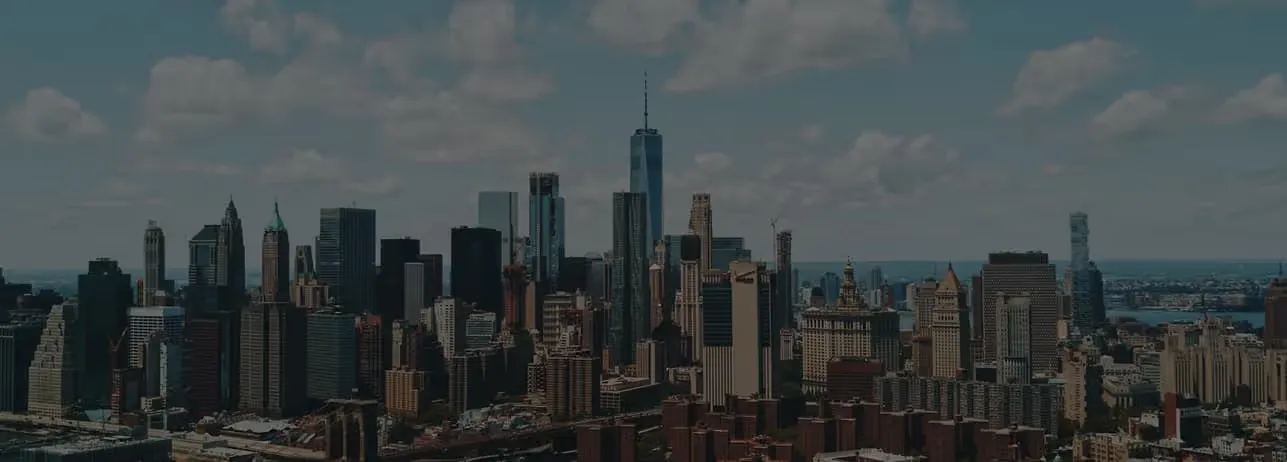 Panoramablick auf die Skyline von New York City mit dem One World Trade Center unter einem teils bewölkten Himmel.